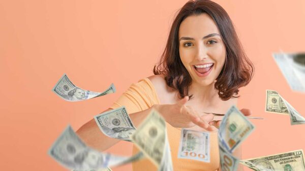 mulher jovem sorrindo de jogando notas de dollars que estava em sua mão em fundo salmão