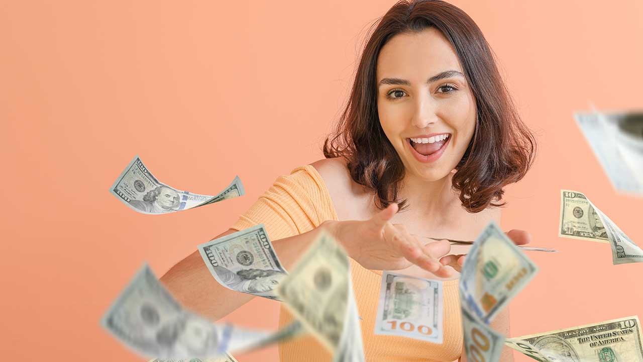 mulher jovem sorrindo de jogando notas de dollars que estava em sua mão em fundo salmão