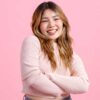 mulher jovem com traços asiáticos sorrindo em fundo rosa