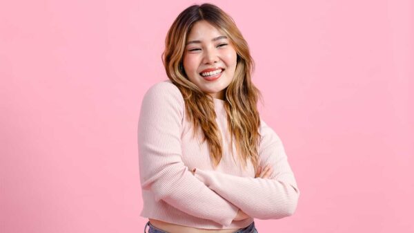mulher jovem com traços asiáticos sorrindo em fundo rosa