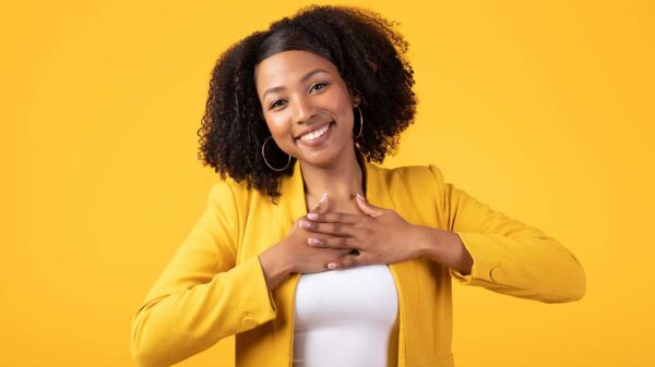 mulher negra sorrindo com as mãos no peito em fundo amarelo