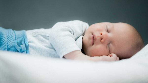 imagem de um bebê deitado dormindo em cama branca e fundo cinza