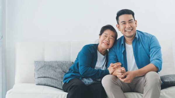 mãe e filhos da descendência asiática sentados num sofá branco em uma sala de parede também branca