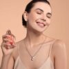 mulher espirando perfume no pescoço e sorrindo em fundo salmão