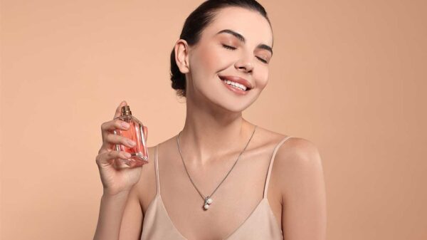 mulher espirando perfume no pescoço e sorrindo em fundo salmão