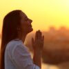 mulher em mãos de prece em seu aberto em pôr do sol