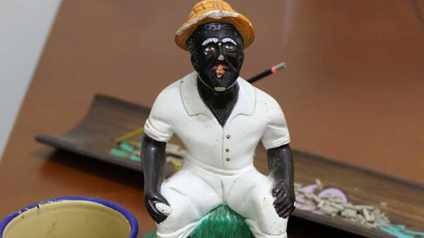 imagem de um preto velho em cima de uma mesa de madeira com um incensário atrás e uma caneca de café na frente