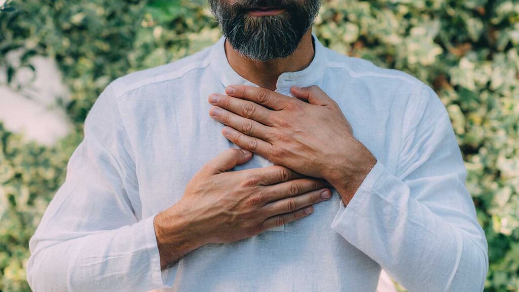 fotografia de um homem vestindo roupa branca e com as mãos no feito em um fundo verde e florido