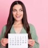 mulher olhando para o lado e sorrindo enquanto segura um calendário em fundo rosa