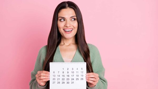 mulher olhando para o lado e sorrindo enquanto segura um calendário em fundo rosa