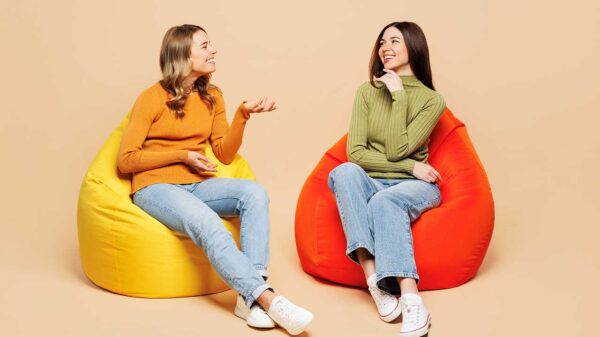 duas amigas sentadas cada uma em um puff vermelho conversando em fundo salmão