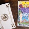 carta do tarot os enamorados ao lado de um deck branco de tarot em cima de uma mesa de madeira